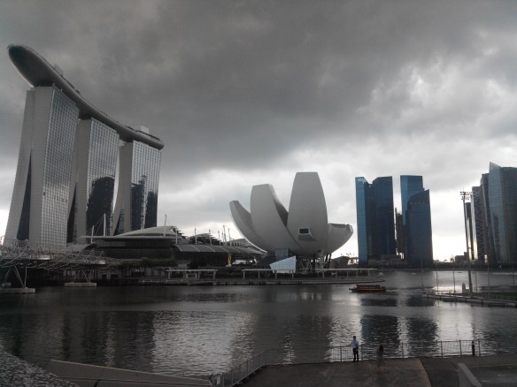 Singapour – Marina Bay Sands et Lotus musée des sciences. Le Marina Bay Sands est un hôtel de 2560 chambres. Il abrite un casino et une piscine à débordement posée sur le dernier étage, le tout sis à côté d’un immense centre commercial où se côtoient les enseignes de luxe. Il est le symbole de la démesure de Singapour mais a pour fonction d’accroître la durée moyenne de séjour touristique sur l’ile, de 2.5 à 3 jours…